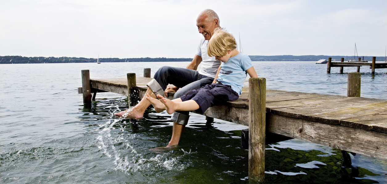 Grandfather and grandchild splash with their feet while sitting on a dock