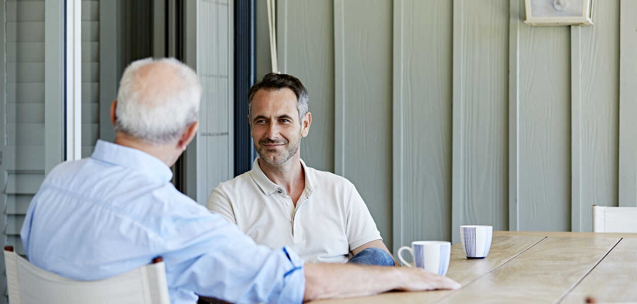 Two men sitting at table chatting with coffees