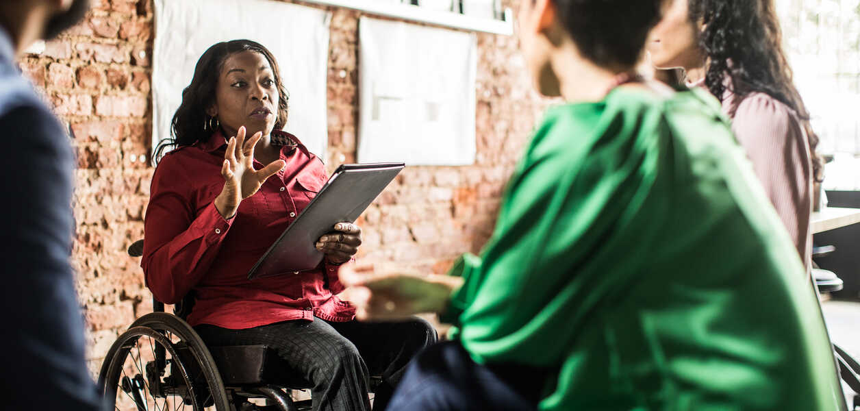 Woman in wheelchair presenting to three people seated around her