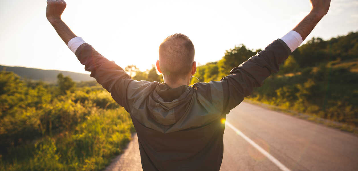  Sport and life achievements and success concept. Sporty man raising arms towards beautiful sunset on the road