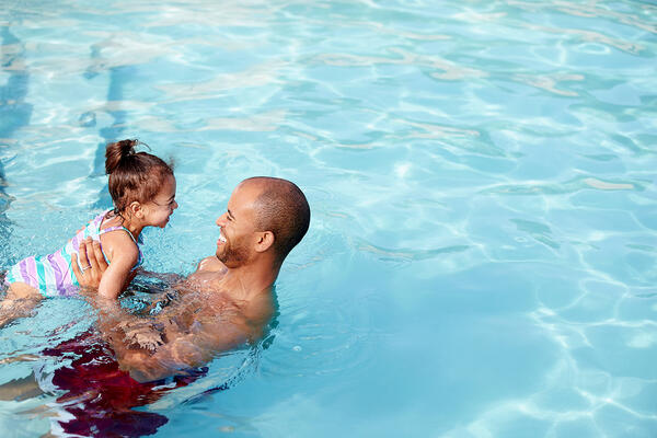 Père heureux apprenant à nager à sa fille dans une piscine