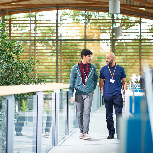 Two male co-workers walking & talking in a open concept office