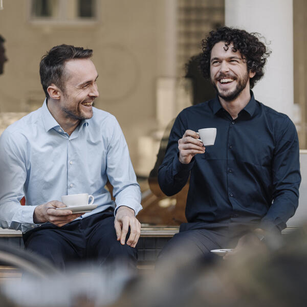 Deux hommes qui rient, tout en prenant un espresso à l’extérieur